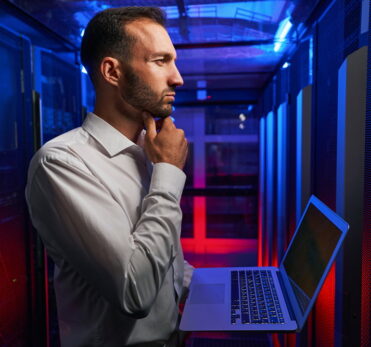 Thoughtful system administrator with laptop in hands looking to the server rack