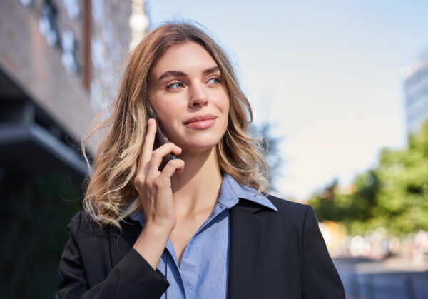 Close up portrait of smiling saleswoman, successful female manager having phone call, answer telephone and walking on street.